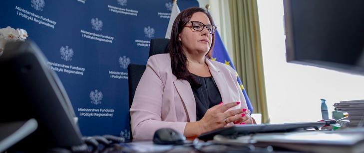 Minister Małgorzata Jarosińska-Jedynak siedzi przy biurku. Za plecami ścianka z logo MFiPR.